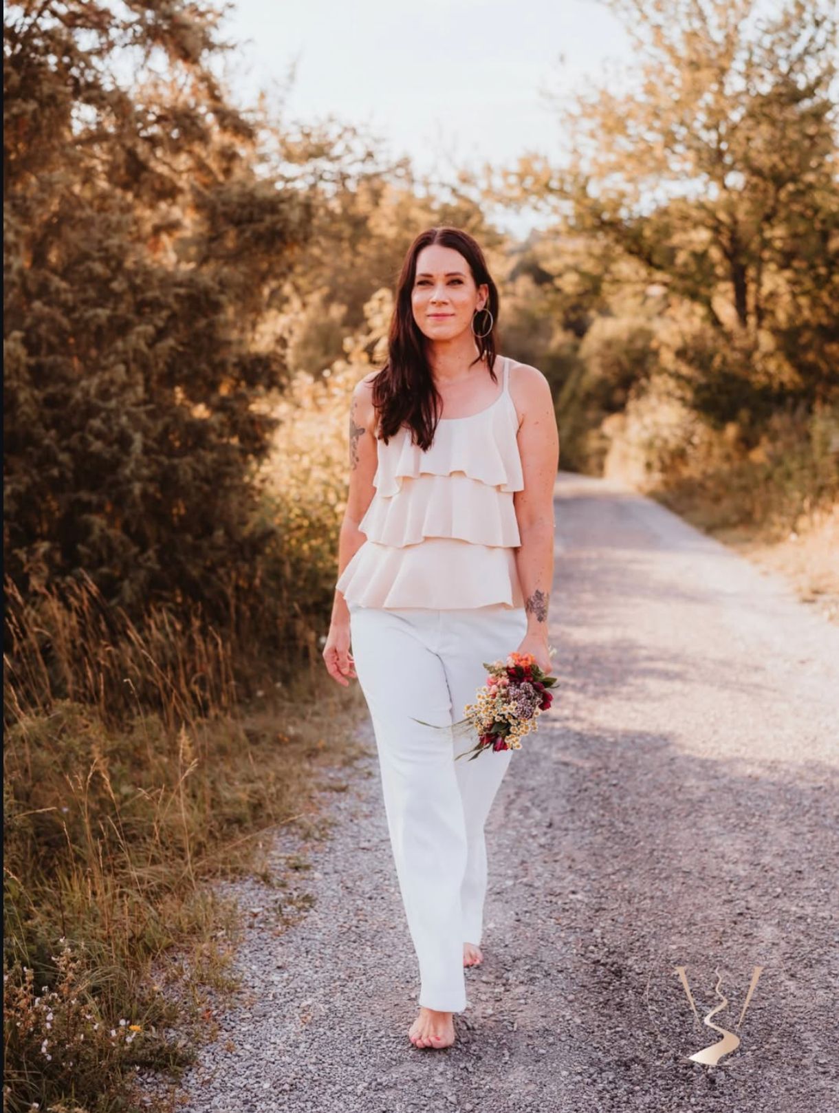 Sonja Mangold geht barfuß über einen Feldweg und hält einen Blumenstrauß